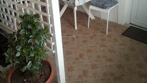 Un pequeño patio con una mesa y sillas blancas, una planta en maceta y decoración mural.