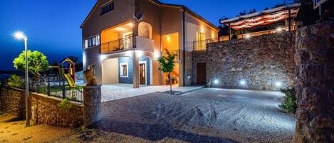 A two-story house with a stone facade, a balcony, and a well-lit entrance.