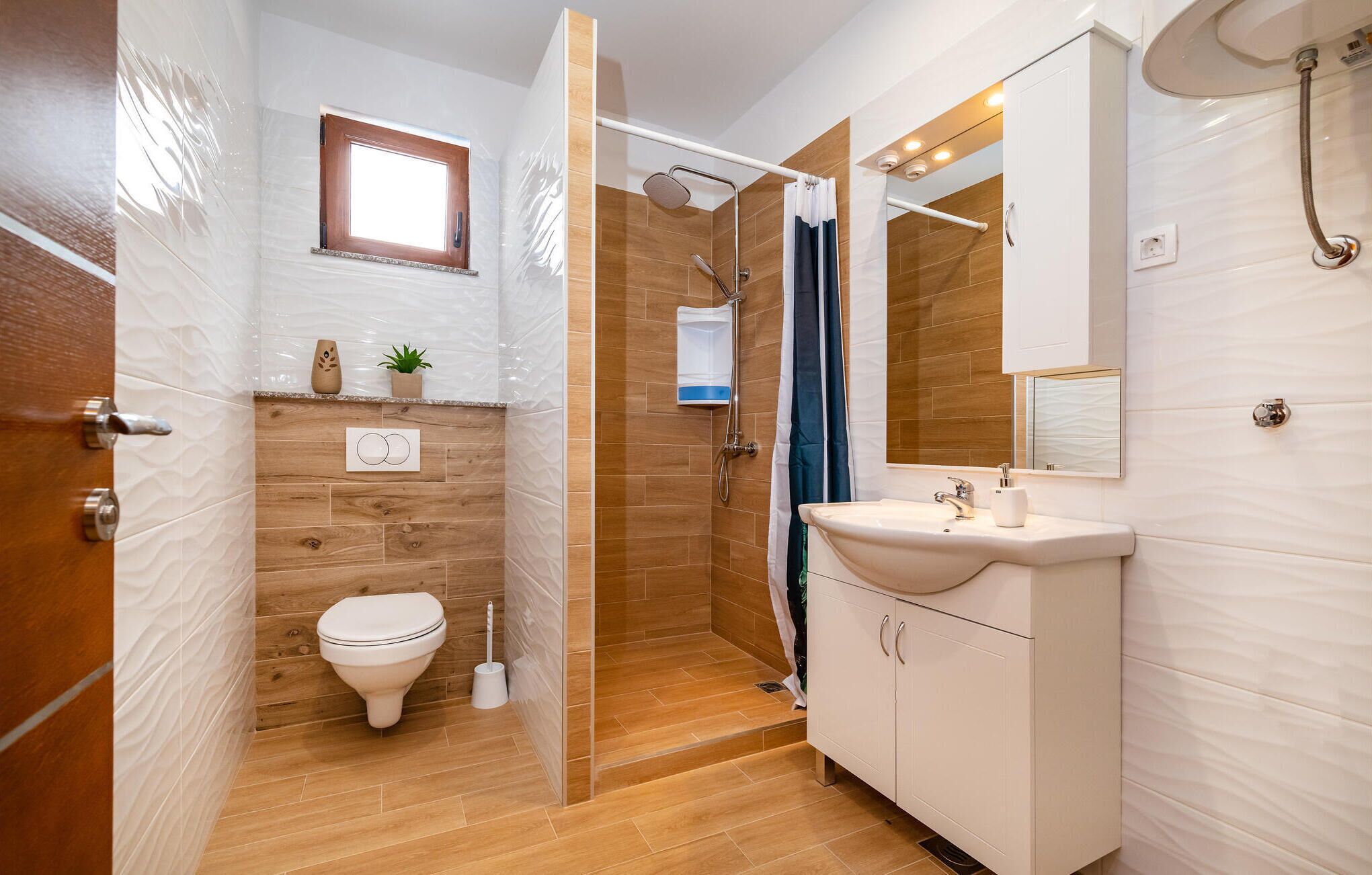 A bathroom with a toilet, sink, shower, and wooden flooring.