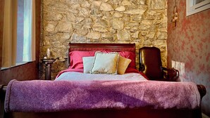 A bedroom with a stone wall, a bed with a red headboard, and a chair.