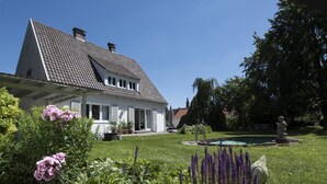 Une maison avec un toit en pente, un porche à l’avant et une piscine dans le jardin.
