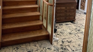 Un escalier en bois, doté d’une rampe, mène à une pièce où se trouve une commode en bois et un sol carrelé.