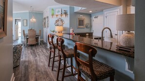 Une cuisine avec un coin bar, des chaises en bois, un lustre et une grande fenêtre.