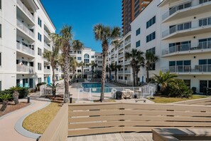 A multi-story hotel with balconies, a swimming pool, and palm trees.