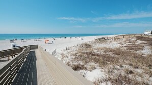 Une plage avec une promenade en bois, des dunes de sable et un ciel bleu dégagé.