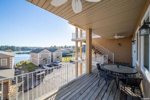 Un balcon donnant sur un lac, un espace couvert avec une table et des chaises, et un escalier menant à un niveau supérieur.