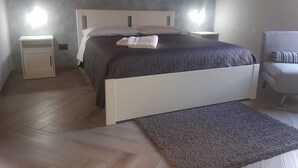 Ein Schlafzimmer mit einem Bett, Nachttischen, einem Sessel und einem Fußboden mit Fischgrätmuster.