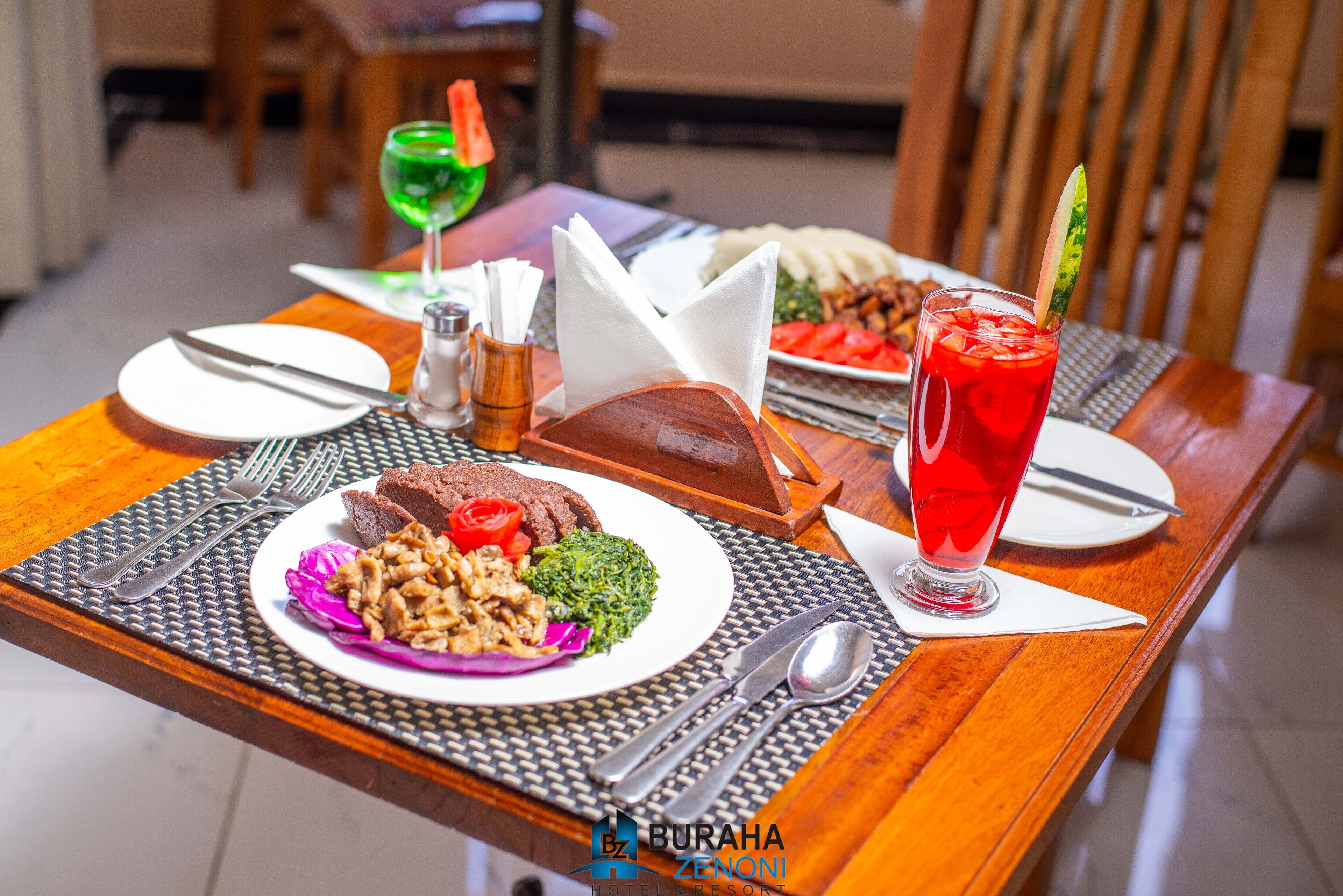A dining table with a meal, including a plate of food, a glass of red drink, and a green drink.