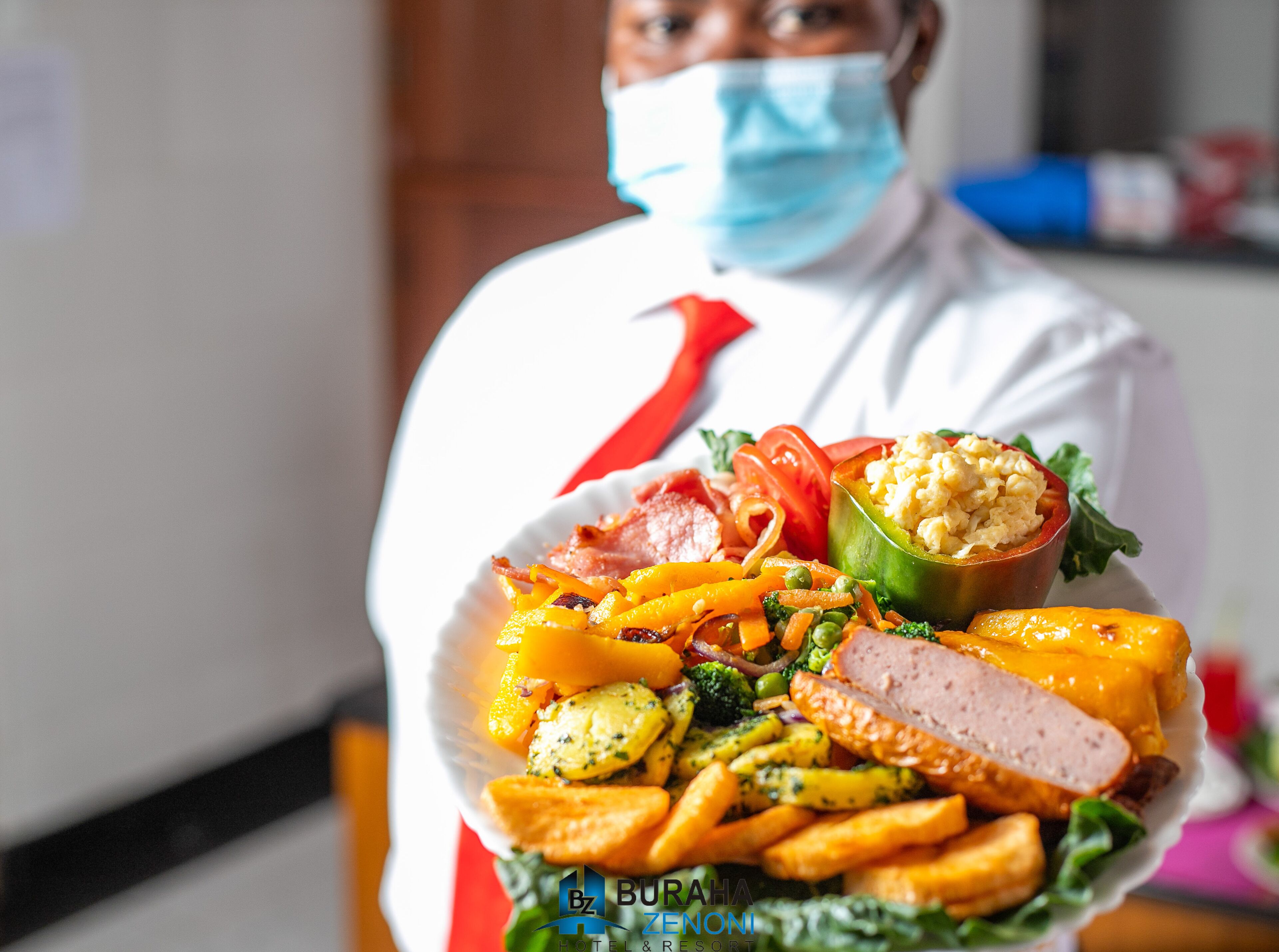A person holding a plate with a variety of foods including vegetables, meat, and a stuffed pepper.