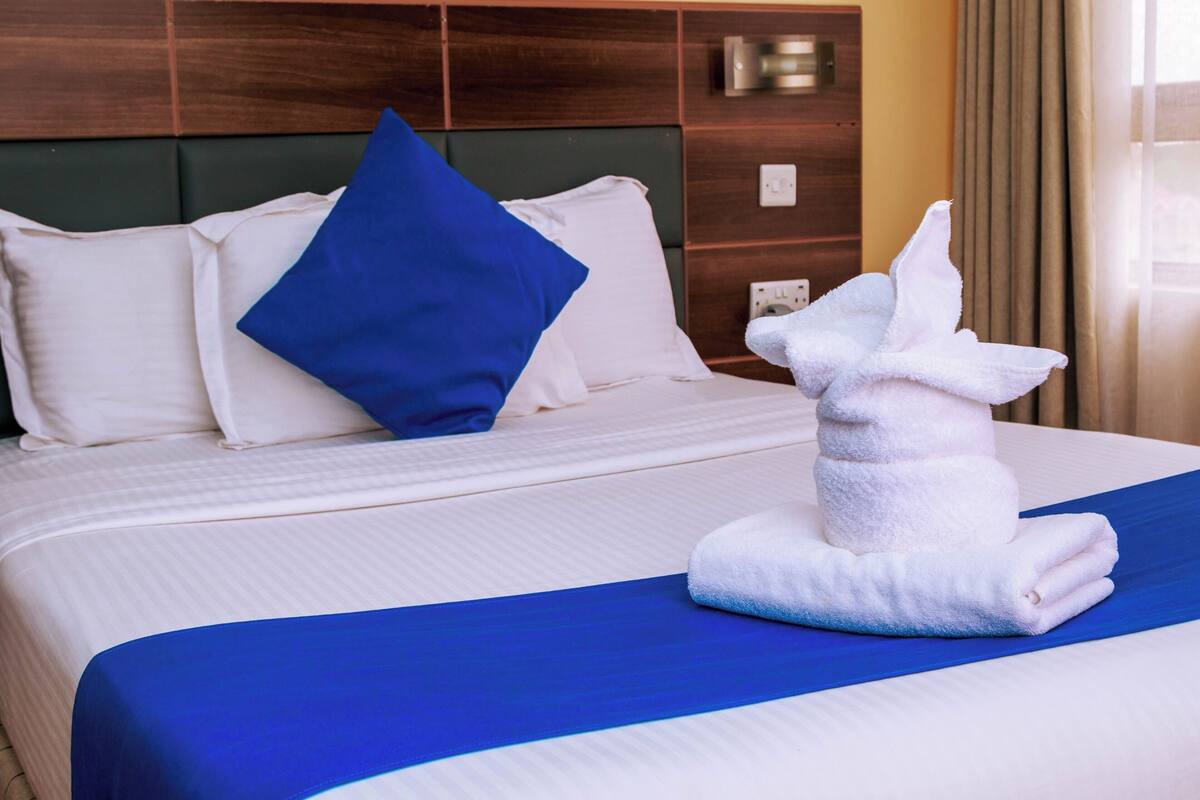 A neatly made bed with white and blue bedding, a blue pillow, and a white towel shaped like a bunny.