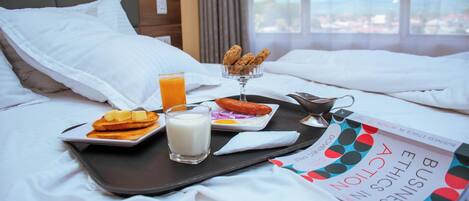 A neatly made bed with white linens, a tray with breakfast items including toast, a glass of orange juice, and a small bowl of cereal.