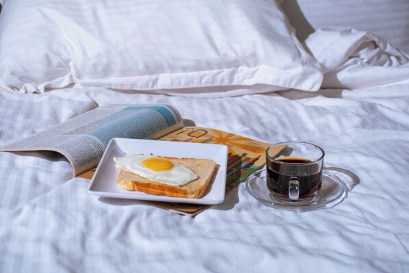 A bed with white linens, a plate with toast and egg, a cup of coffee, and a newspaper.
