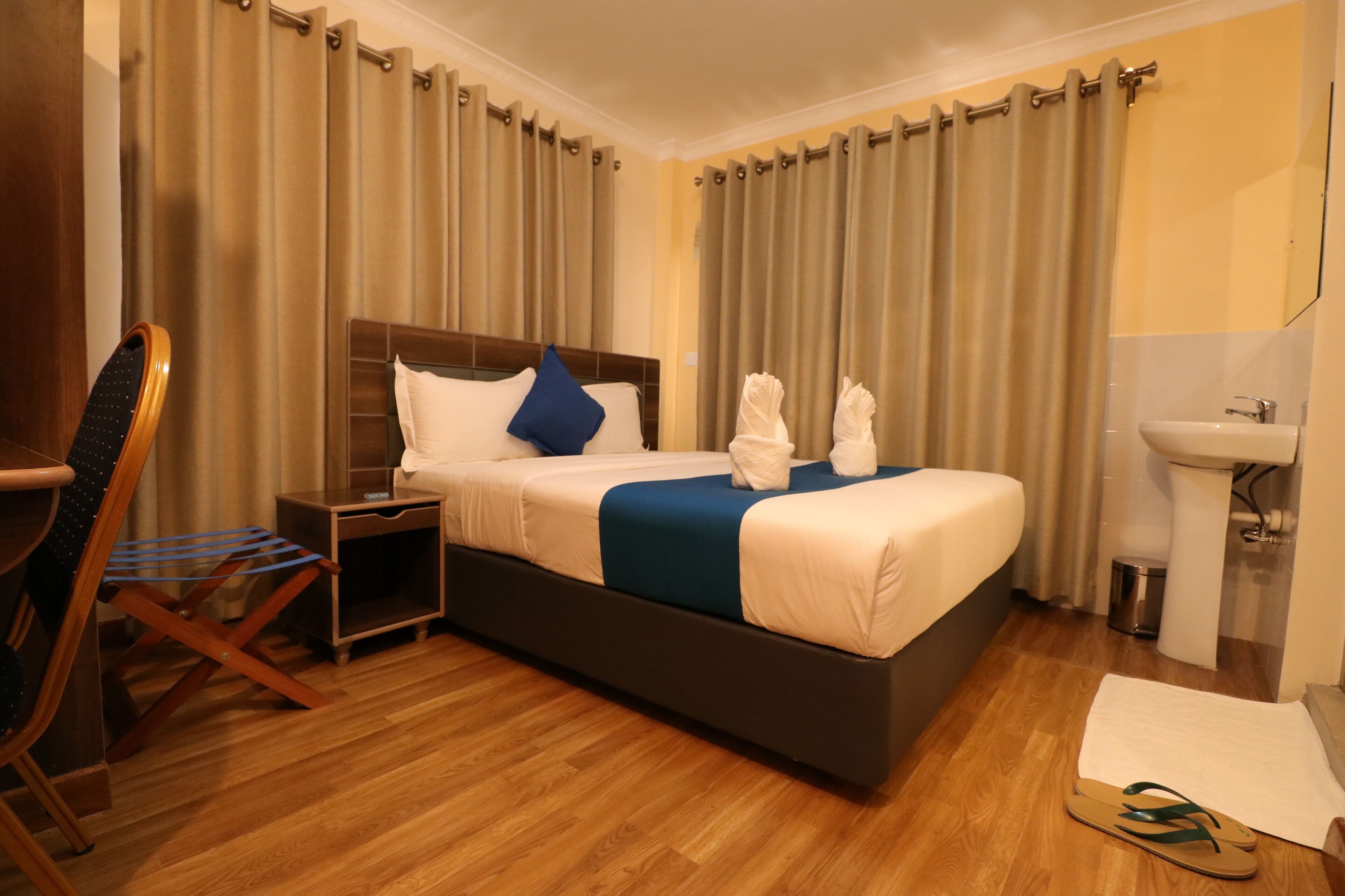 A hotel room with a bed, a nightstand, a chair, a sink, and a mirror.