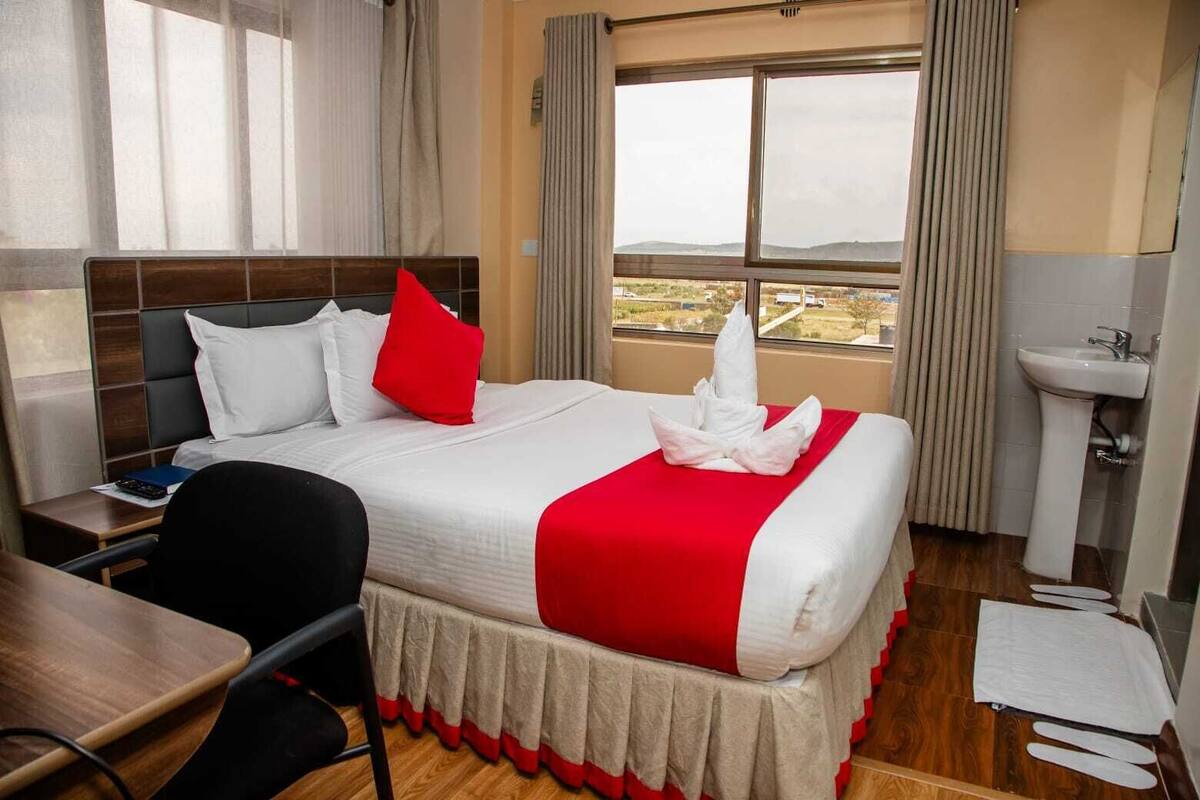 A hotel room with a bed, a desk, a chair, a sink, and a view of the landscape.