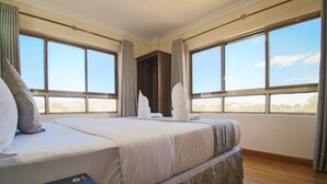 A hotel room with a large bed, two windows, and a view of the city.