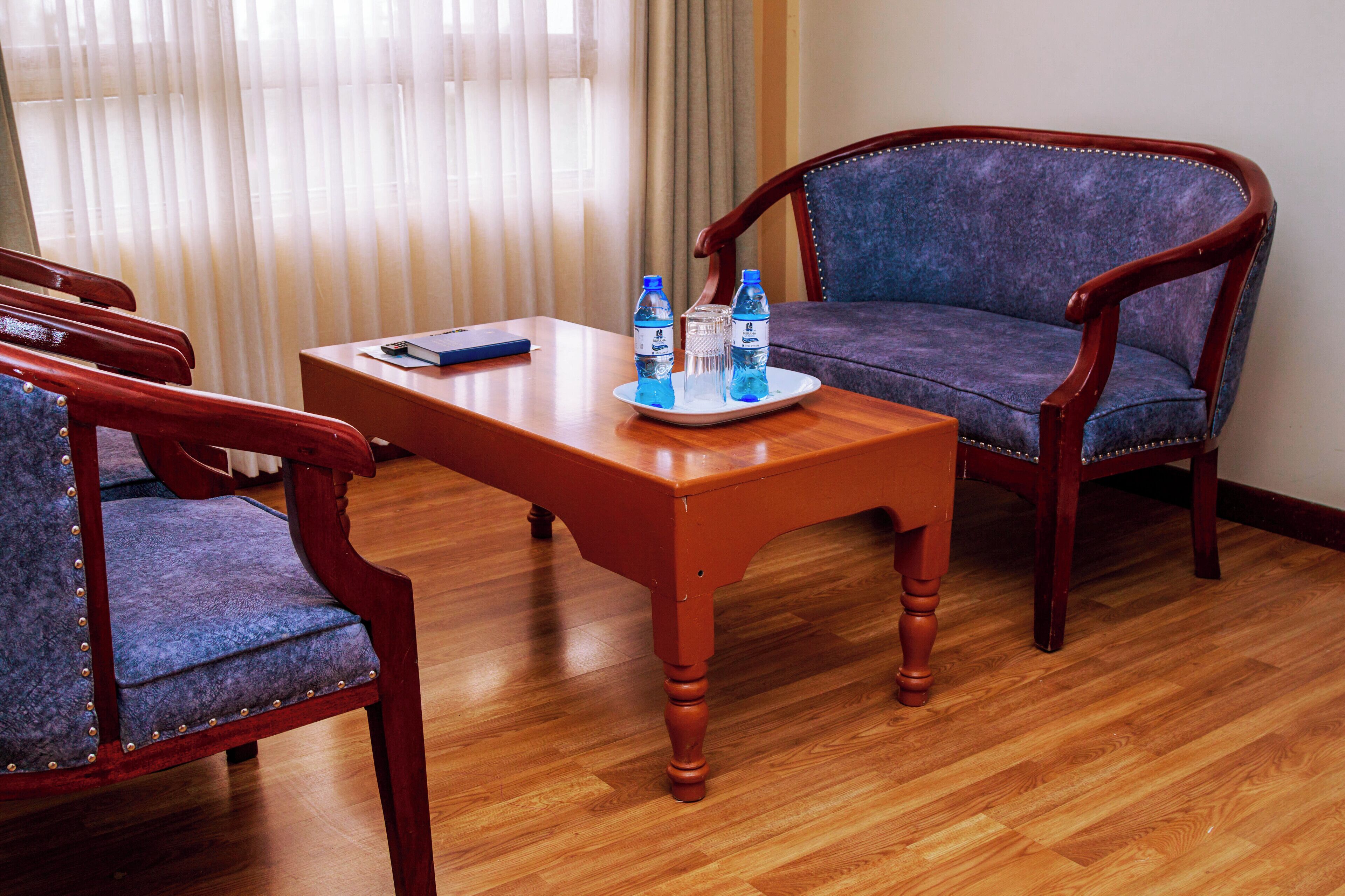 Een kamer met een houten tafel, twee blauwe fauteuils en een blauwe bank. Op de tafel staan twee waterflesjes en een glas.