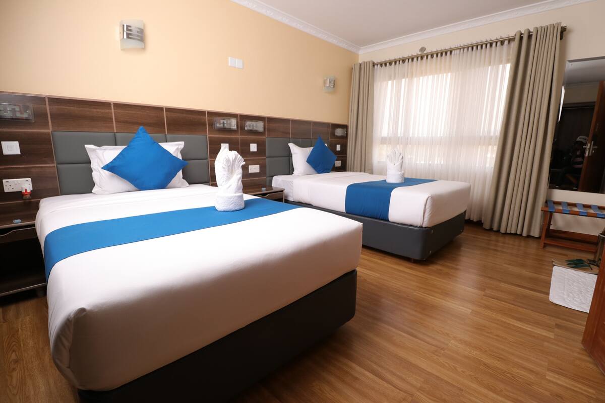 A hotel room with two beds, wooden flooring, and a large window with curtains.