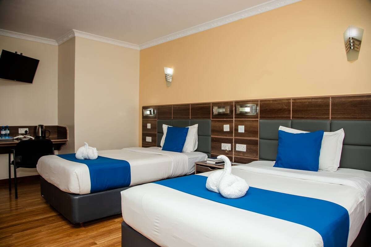A hotel room with two beds, a desk, and a television.