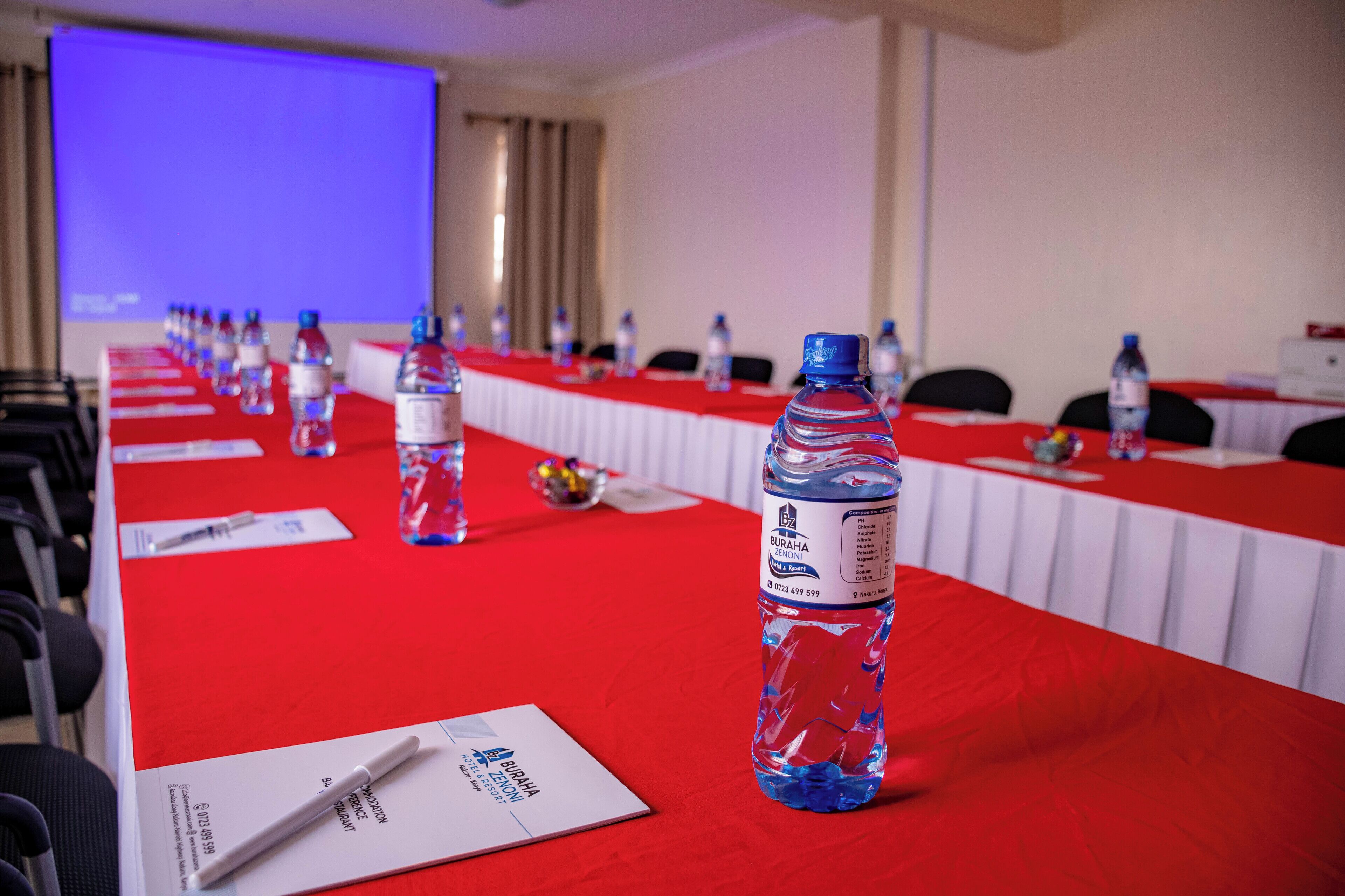 A conference room with a long table covered in a red tablecloth, water bottles, and name cards.