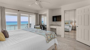 Un dormitorio con cama, escritorio, silla, televisor y una puerta que da a otra habitación.