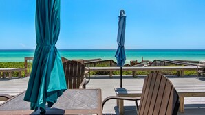 Una terraza de madera con sillas y mesas con vista a la playa.