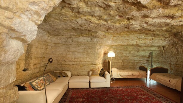 A cozy room with a stone ceiling, a sofa, a bed, and a red rug.