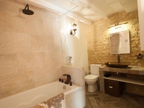 Un baño con bañera, inodoro, lavabo con lavamanos y cabezal de ducha.