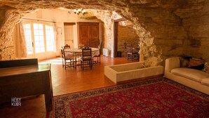 A cozy stone-walled room with a round dining table, chairs, and a red patterned rug.
