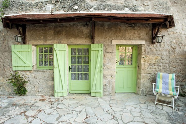 A rustic stone building with green shutters and a small porch area.