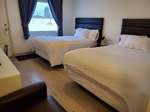 Una camera d'albergo con due letti, una scrivania e una finestra con tende.