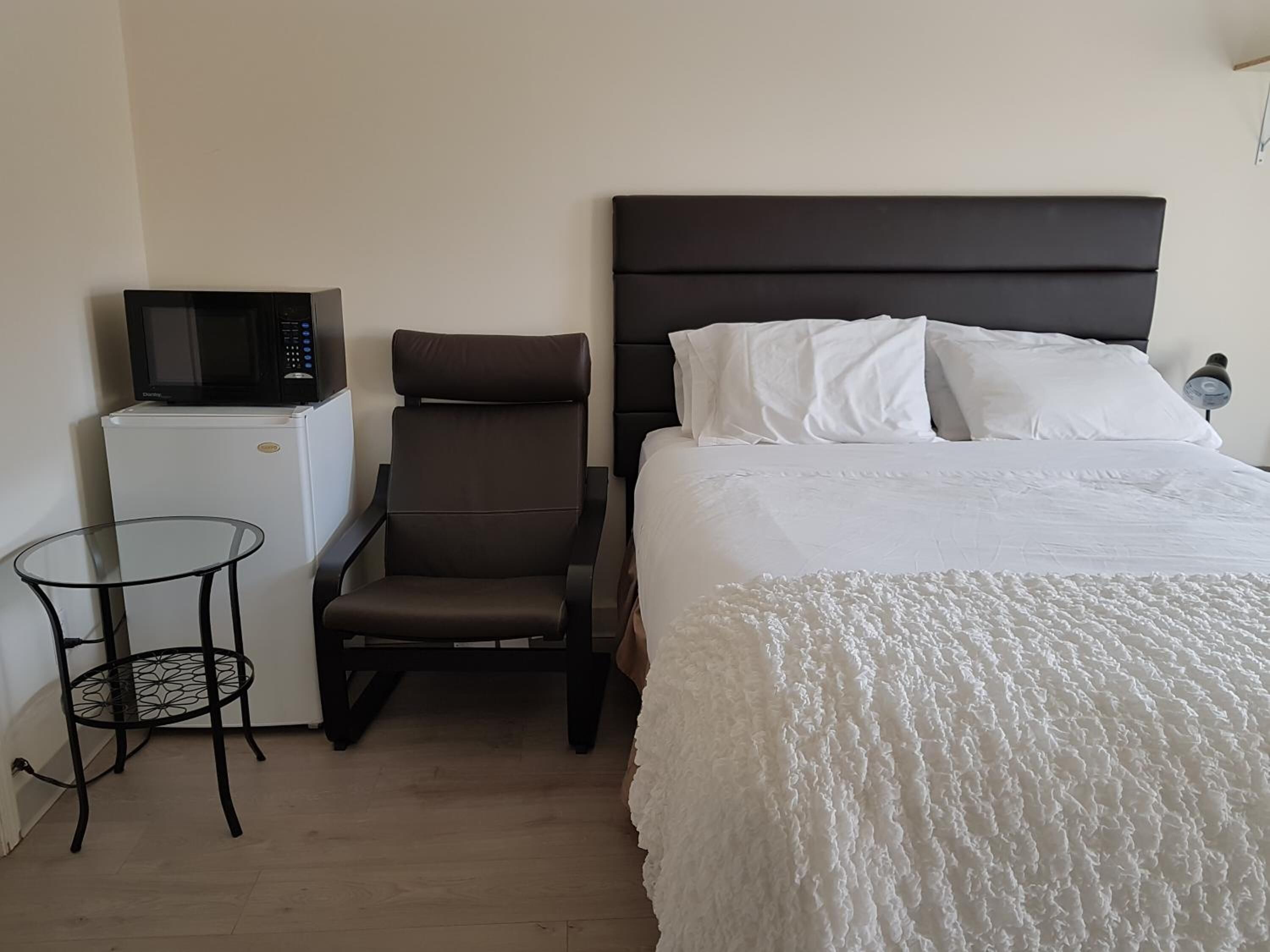 A hotel room with a bed, a chair, a small table, a microwave, and a refrigerator.
