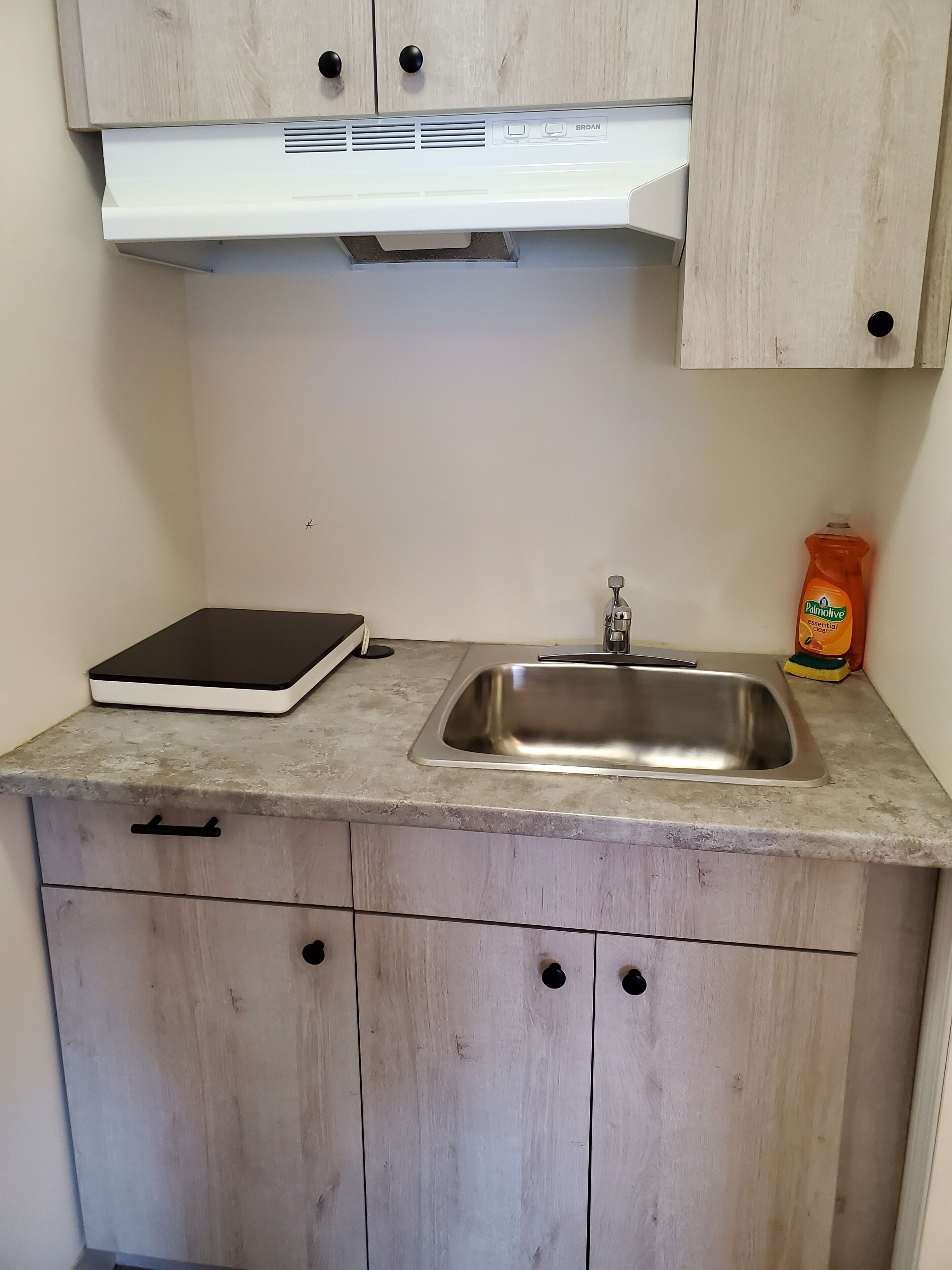 Een keuken met een roestvrijstalen spoelbak, een witte afzuigkap en een houten kastje met twee lades.