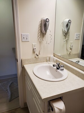 Un bagno con un lavandino, un asciugacapelli fissato alla parete e uno specchio.