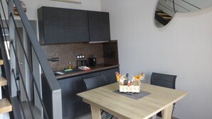 Une cuisine moderne avec des meubles de couleur sombre, une table à manger en bois et une œuvre d’art murale représentant un cactus.