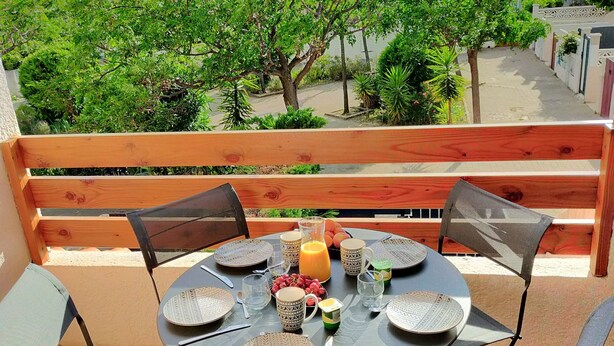 Une table ronde dressée pour six personnes, avec des assiettes à motifs, des verres et une carafe de jus d’orange.