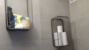 Une salle de bain avec deux paniers en fil métallique accrochés au mur, l’un contenant des articles de toilette et l’autre du papier toilette.