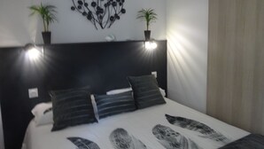 Une chambre à coucher moderne avec une tête de lit noire, deux plantes en pot et un lit agrémenté d’oreillers à rayures.