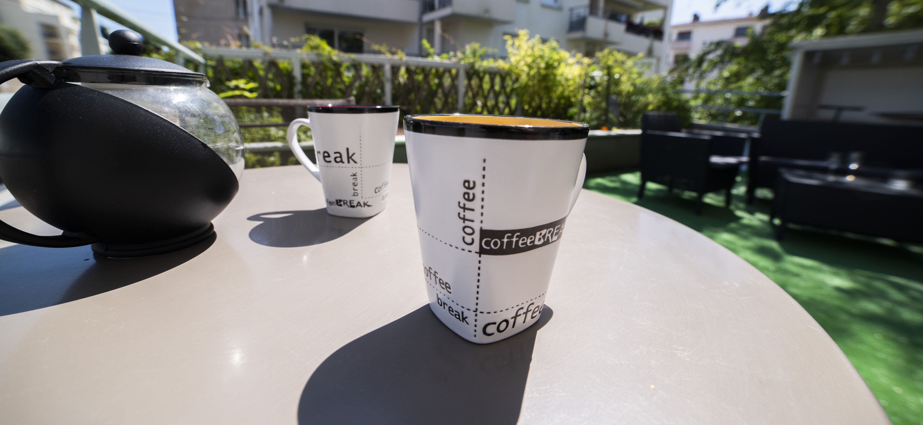Une table avec une cafetière et deux tasses à café, sur lesquelles est inscrit le texte « pause-café ».