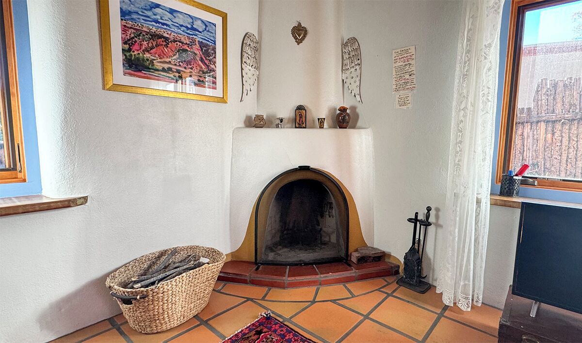 A cozy room with a fireplace, a basket of firewood, and a window with a view of a building.