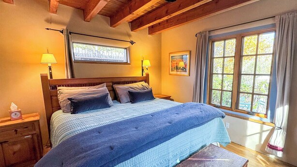 Een slaapkamer met een groot bed, twee bedlampen, een raam met gordijnen en een houten plafond.