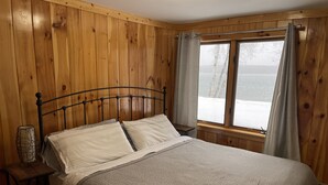 Ein Zimmer mit Holzwänden, einem Bett, einem Nachttisch und einem Vorhangfenster.