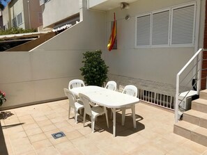 Eine Terrasse mit einem weißen Tisch und Stühlen, einem Topfpflanzen und einer Flagge.