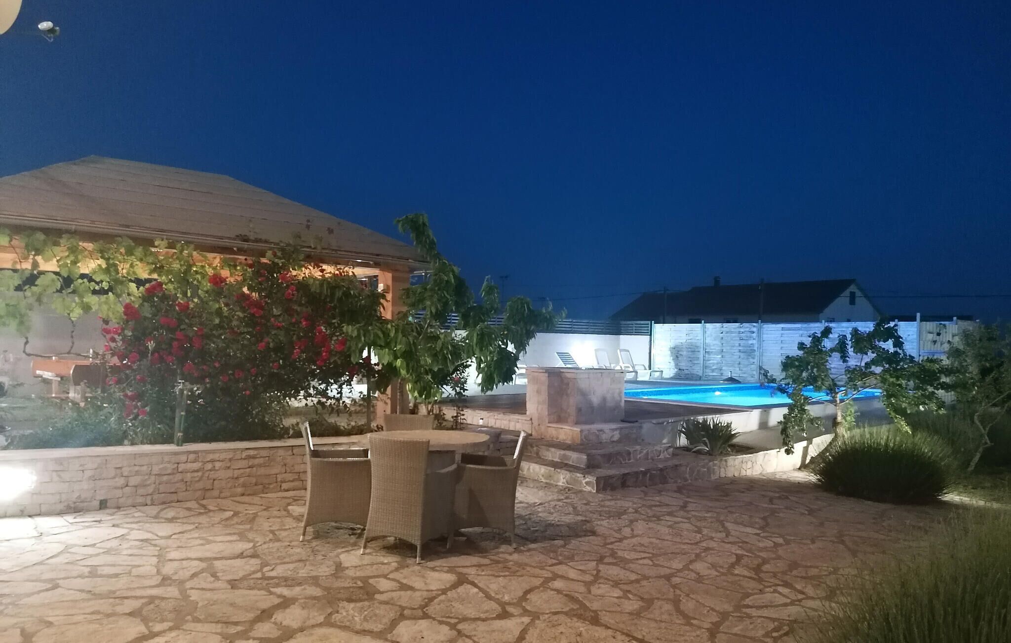 Un'area patio esterna con pavimento in pietra, una piscina e una zona salotto coperta con sedie.