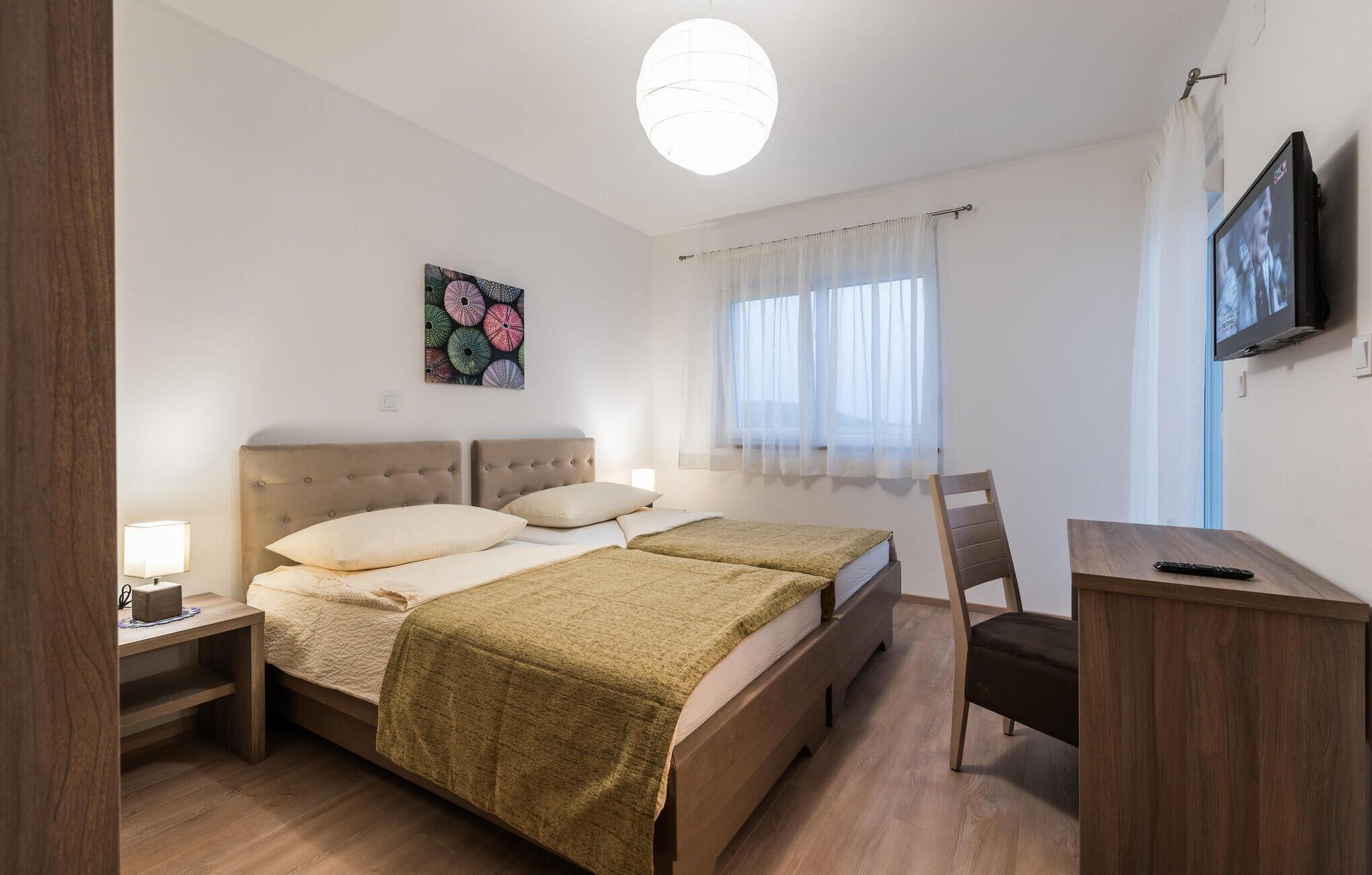 Une chambre d’hôtel comprenant un lit, une table de chevet, une chaise, un bureau, une télévision et une fenêtre avec des rideaux.