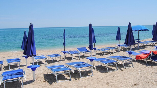 A beach with rows of blue lounge chairs and matching umbrellas, arranged on a sandy shore. - Soc.Agr.IL VERDE s..s (Apecchio)