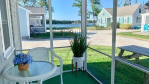 Ein überdachter Außenbereich mit Tisch und Stühlen, einem Blumentopf und Blick auf einen See sowie Häuser im Hintergrund.