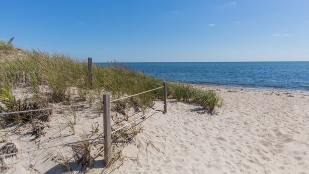 Ein sandiger Strand mit Holzzaun und Gras.