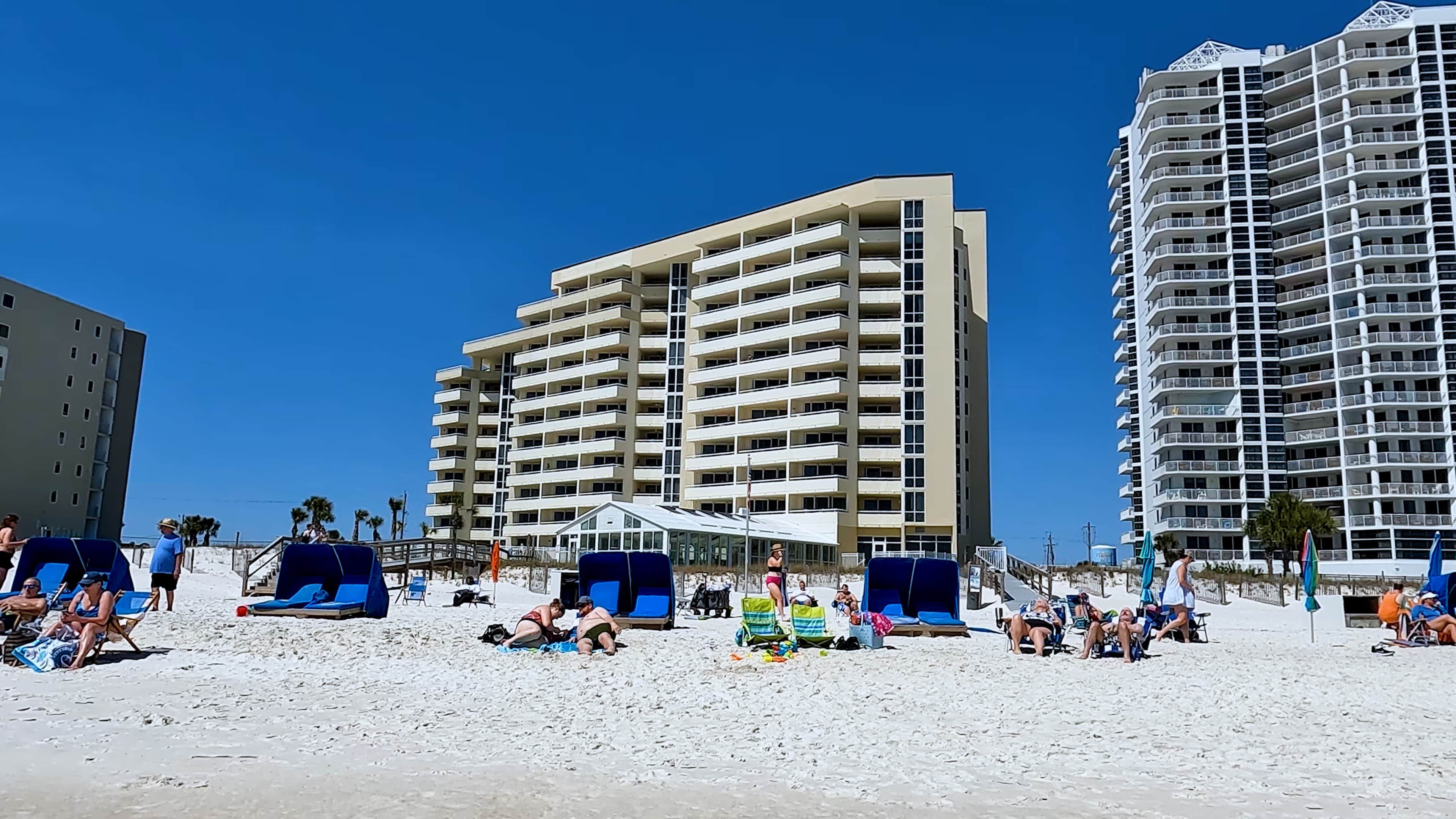 A beachfront hotel with multiple floors, outdoor seating, and a clear sky.