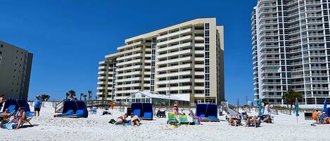 A beachfront hotel with multiple floors, outdoor seating, and a clear sky.