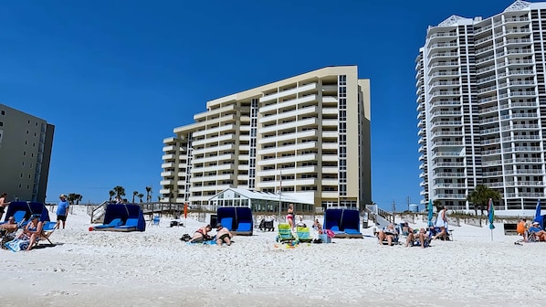 A beachfront hotel with multiple floors, outdoor seating, and a clear sky.